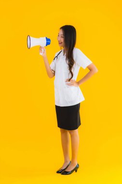 Güzel bir Asyalı genç doktor portresi. Sarı izole arka planda megafon kullanıyor.