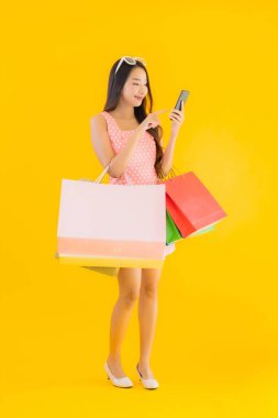 Renkli alışveriş çantalı güzel Asyalı kadın akıllı cep telefonu ve sarı izole edilmiş arka planda kredi kartı.