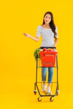 Sarı izole edilmiş arka planda, süpermarketten alışveriş sepeti taşıyan güzel Asyalı kadın portresi