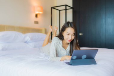Güzel bir Asyalı kadının portresi yatak odasının içinde kredi kartıyla tablet kullanıyor.