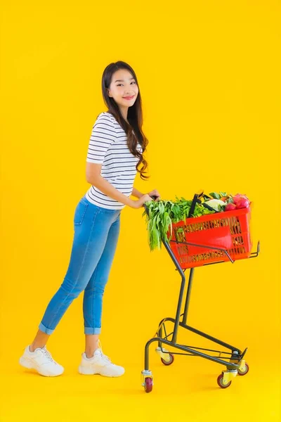 노란색외진 배경에 슈퍼마켓 카트에서 식료품을 아름다운 아시아 여자의 — 스톡 사진
