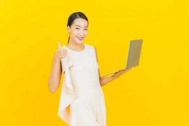 Asyalı güzel bir kadının portresi. Sarı izole edilmiş arka planda dizüstü bilgisayarla gülümsüyor.