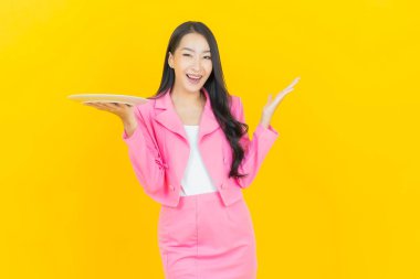 Asyalı güzel bir kadının portresi. Sarı arka planda boş tabak tabağıyla gülümsüyor.