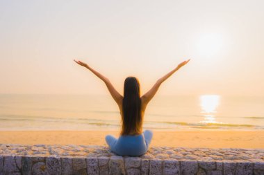 Genç Asyalı kadının portresi sağlık için gün doğumunda deniz kıyısı okyanusunda meditasyon yapıyor.