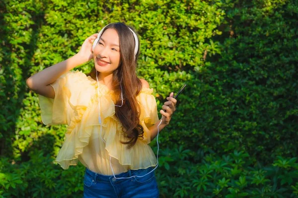 年轻的亚洲女人使用智能手机和耳机聆听户外花园自然景观的音乐 — 图库照片