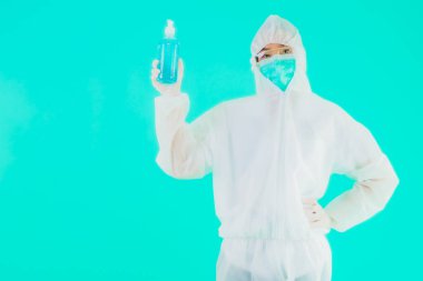 Güzel bir portre genç Asyalı doktor. Özel süit ve maske takıyor. Alkol jeli ve mavi izole bir arka plan.