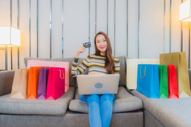 Asyalı güzel bir kadının portresi kanepeye dizüstü bilgisayar kullanıyor.