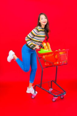 Marketten aldığı alışveriş sepetiyle kırmızı izole arka planda güzel bir Asyalı kadın portresi.