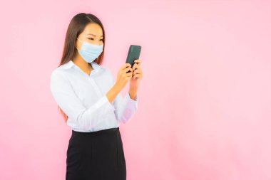 Güzel Asyalı bir kadının portresi, pembe arka planda Covid19 ve Coronavirus 'tan korunmak için maske takar.