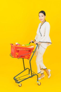 Sarı arka planda süpermarketten alışveriş sepeti almış güzel genç Asyalı kadın portresi.