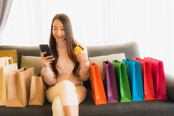 아름다운 아시아 거실에 쇼핑백 주위에서 온라인 쇼핑을 노트북이나 스마트폰을 사용하는 — 스톡 사진