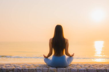 Genç Asyalı kadının portresi sağlık için gün doğumunda deniz kıyısı okyanusunda meditasyon yapıyor.