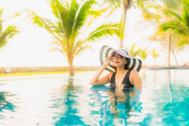 Güzel bir Asyalı kadın portresi, gün batımında palmiye ağacıyla birlikte havuz kenarında dinleniyor ya da tatil için gün doğumunda dinleniyor.