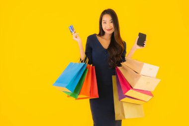 Portre güzel genç Asyalı kadın alışveriş çantası kredi kartı ve akıllı cep telefonu sarısı izole bir arka plan.