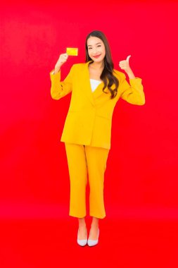 Güzel bir Asyalı kadının portresi kırmızı arka planda kredi kartıyla cep telefonu kullanıyor.