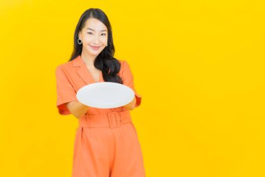 Asyalı güzel bir kadının portresi. Sarı arka planda boş tabak tabağıyla gülümsüyor.