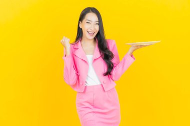 Asyalı güzel bir kadının portresi. Sarı arka planda boş tabak tabağıyla gülümsüyor.