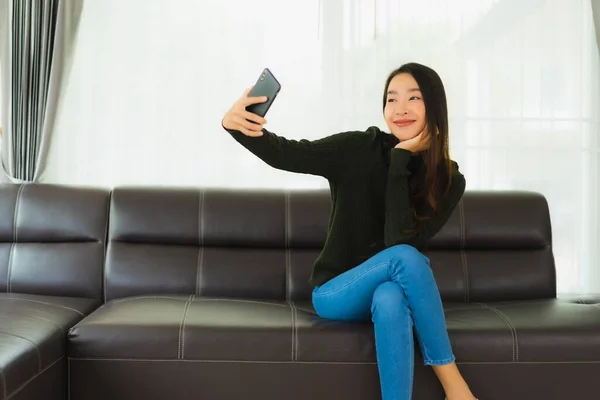漂亮的年轻亚洲女人在客厅的沙发上使用智能手机或手机 — 图库照片