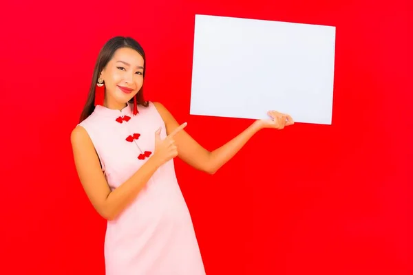美丽的年轻亚洲女人在红色背景上展示白色的空广告牌 — 图库照片