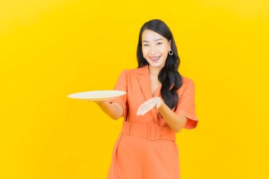 Asyalı güzel bir kadının portresi. Sarı arka planda boş tabak tabağıyla gülümsüyor.