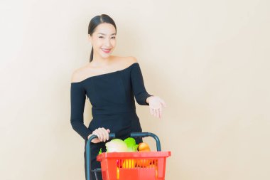 Renkli arka planda süpermarketten alınmış market sepetiyle gülümseyen güzel Asyalı kadın portresi.