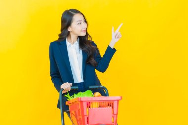 Renkli arka planda süpermarketten alınmış market sepetiyle gülümseyen güzel Asyalı kadın portresi.