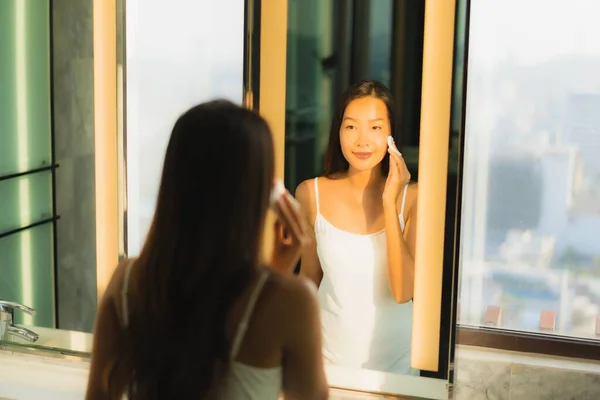 ポートレート美しいです若いですアジアの女性クリーン彼女の顔と顔とともにミラーでバスルームインテリア — ストック写真