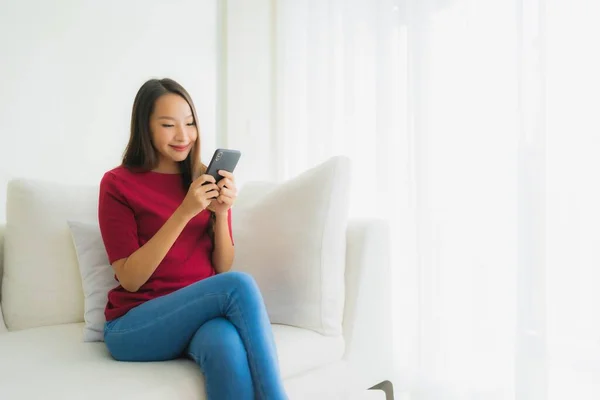 在客厅的沙发上用手机或智能手机描绘美丽的年轻亚洲女人 — 图库照片
