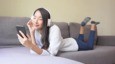 Evde kulaklıkla müzik dinleyen Asyalı güzel bir kadının görüntüleri.