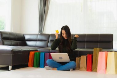 Güzel bir Asyalı kadın portresi evde online alışveriş yapmak için laptop ve kredi kartı kullanıyor.
