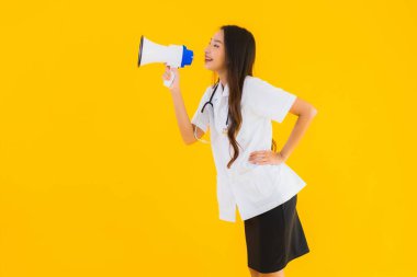 Güzel bir Asyalı genç doktor portresi. Sarı izole arka planda megafon kullanıyor.