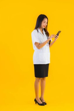Güzel Asyalı genç doktor kadın sarı izole edilmiş arka planda akıllı cep telefonu kullanıyor.