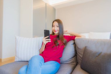 Güzel bir Asyalı kadın portresi. Yatak odasının iç tarafındaki oturma odasındaki koltukta akıllı cep telefonu kullanıyor.