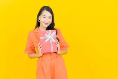 Asyalı güzel bir kadının portresi. Sarı arka planda kırmızı hediye kutusuyla gülümsüyor.