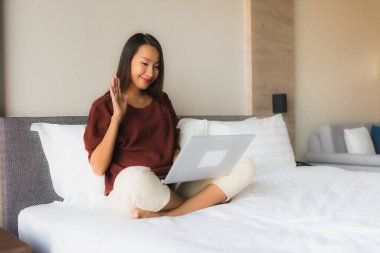 Yatak odasındaki yatakta bilgisayar ve cep telefonu kullanan güzel Asyalı kadınların portresi.