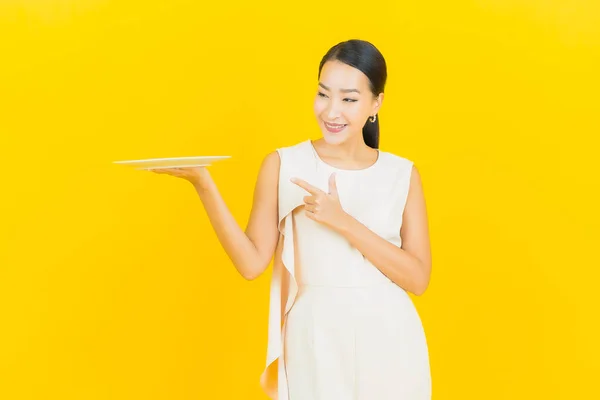 肖像画美しい若いアジアの女性の笑顔とともに空のプレート料理上の黄色の背景 — ストック写真