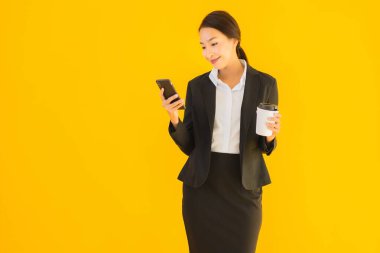 Portre güzel genç Asyalı kadın akıllı cep telefonu ve kahve fincanı ile izole edilmiş sarı arka planda