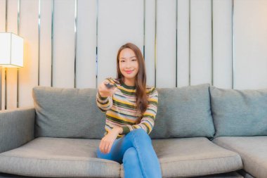 Güzel bir Asyalı kadın oturma odasındaki uzaktan kumandayı kullanıyor.