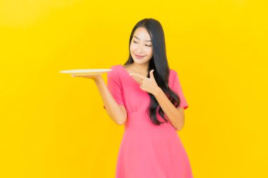 Asyalı güzel bir kadının portresi. Sarı arka planda boş tabak tabağıyla gülümsüyor.