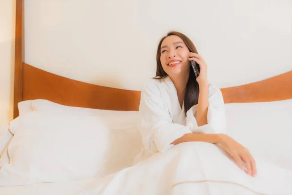 肖像画美しい若いアジアの女性は寝室のインテリアでベッドの上にスマートフォンを使用します — ストック写真