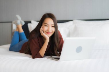 Güzel bir Asyalı kadın yatak odasının iç kısmında bilgisayar kullanıyor.