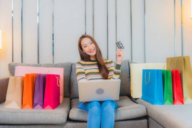 Asyalı güzel bir kadının portresi kanepeye dizüstü bilgisayar kullanıyor.