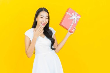 Asyalı güzel bir kadının portresi. Sarı arka planda kırmızı hediye kutusuyla gülümsüyor.