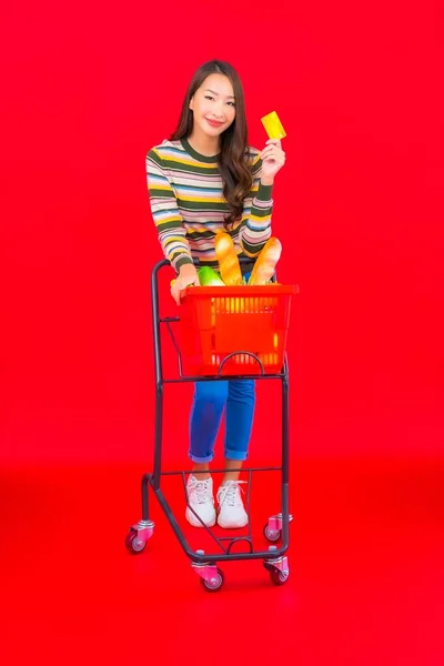 穿着红色孤立背景的超市购物篮的美丽的亚洲年轻女子的画像 — 图库照片