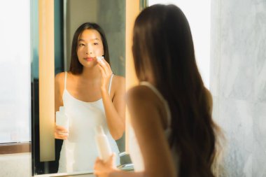 Güzel bir Asyalı kadın portresi. Yüzünü ve yüzünü banyo içinde aynayla temizliyor.