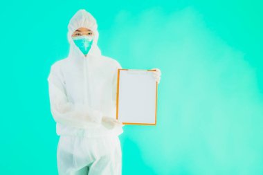 Güzel, genç Asyalı doktor kadın koronavirüsten korunmak için ppe ya da kişisel koruyucu ekipman takıyor ya da mavi izole arka planda beyaz kartı olan 19. bölgede yaşıyor.