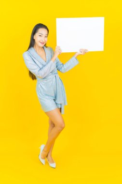 Asyalı güzel bir kadının portresi. Sarı arka planda boş beyaz ilan panosuyla gülümsüyor.