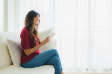 Güzel bir Asyalı kadın portresi oturma odasındaki koltukta kitap okuyor.