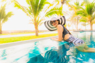 Güzel bir Asyalı kadın portresi, gün batımında palmiye ağacıyla birlikte havuz kenarında dinleniyor ya da tatil için gün doğumunda dinleniyor.