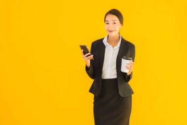 Portre güzel genç Asyalı kadın akıllı cep telefonu ve kahve fincanı ile izole edilmiş sarı arka planda